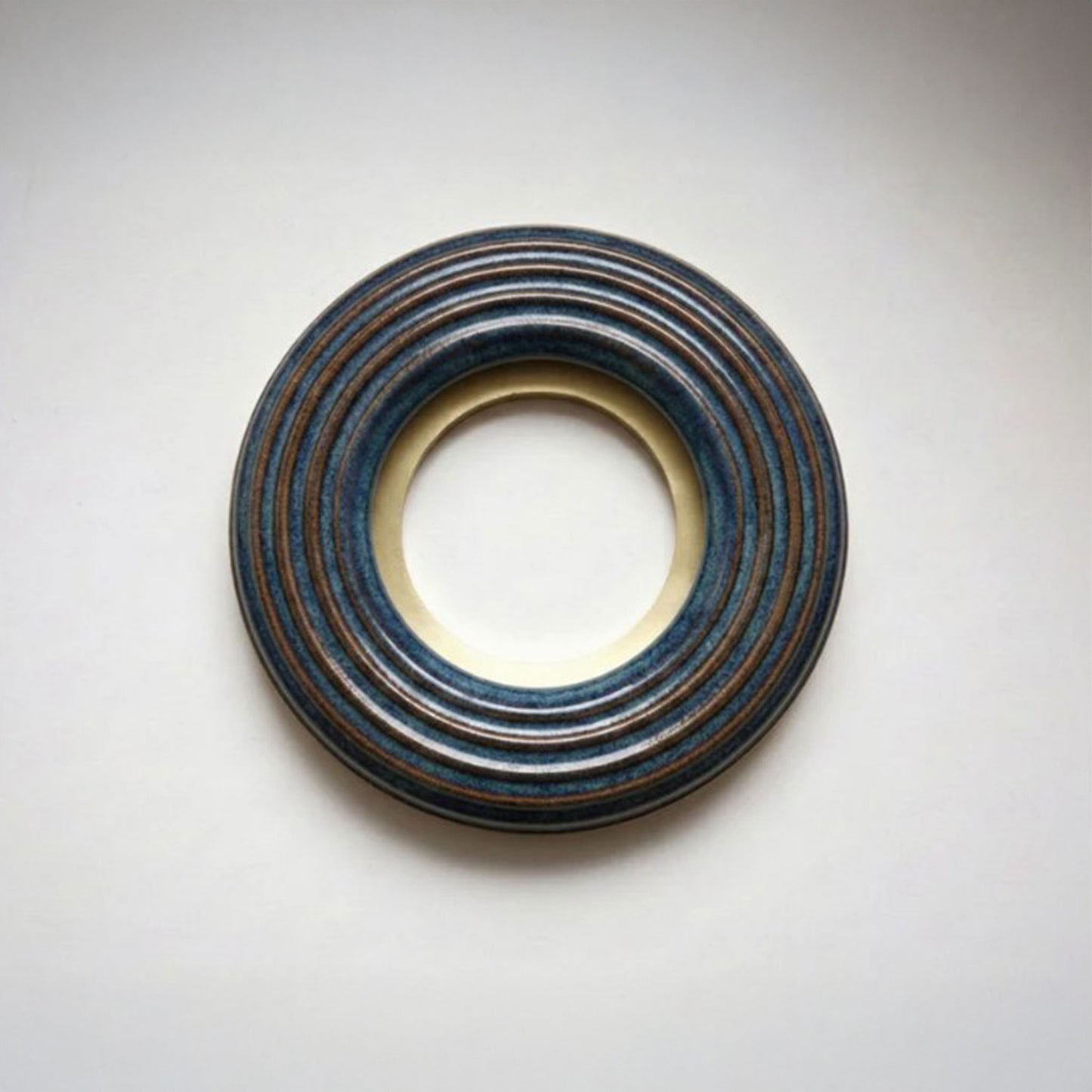 A large donut-shaped blue ribbed ring with a polished gold-toned inner and outer rim, photographed on a light gray background.