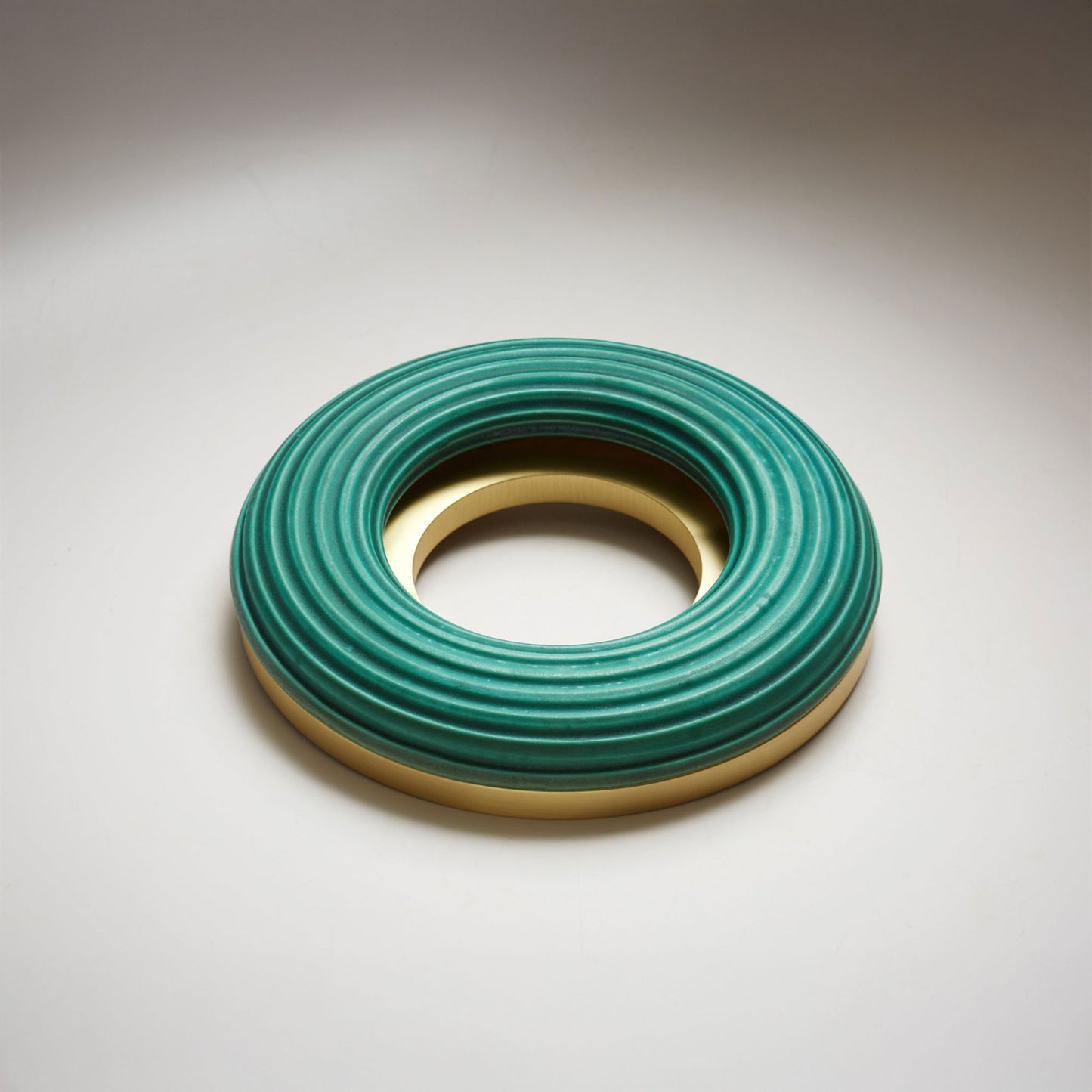 A large donut-shaped teal-green ribbed ring with a polished gold-toned inner and outer rim, photographed on a light gray background.