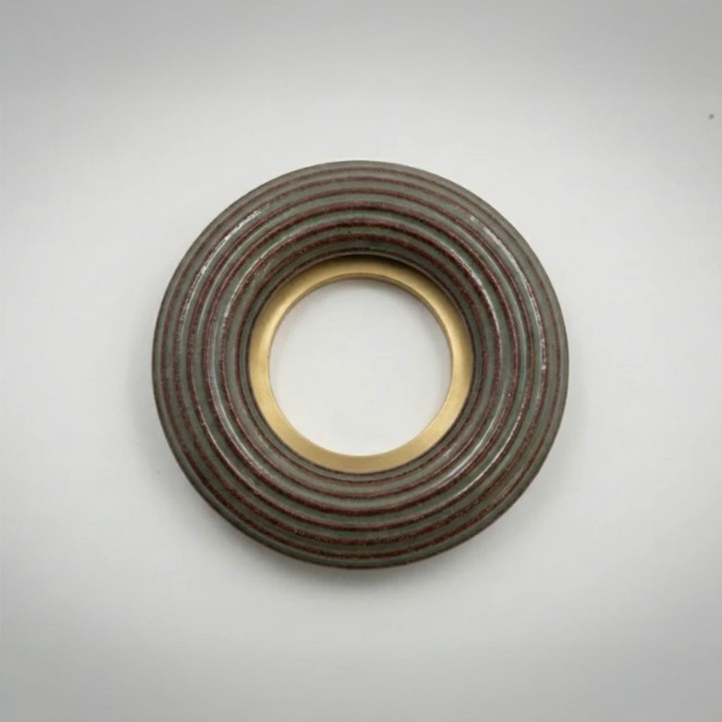 A large donut-shaped sage green terracotta ribbed ring with a polished gold-toned inner and outer rim, photographed on a light gray background.
