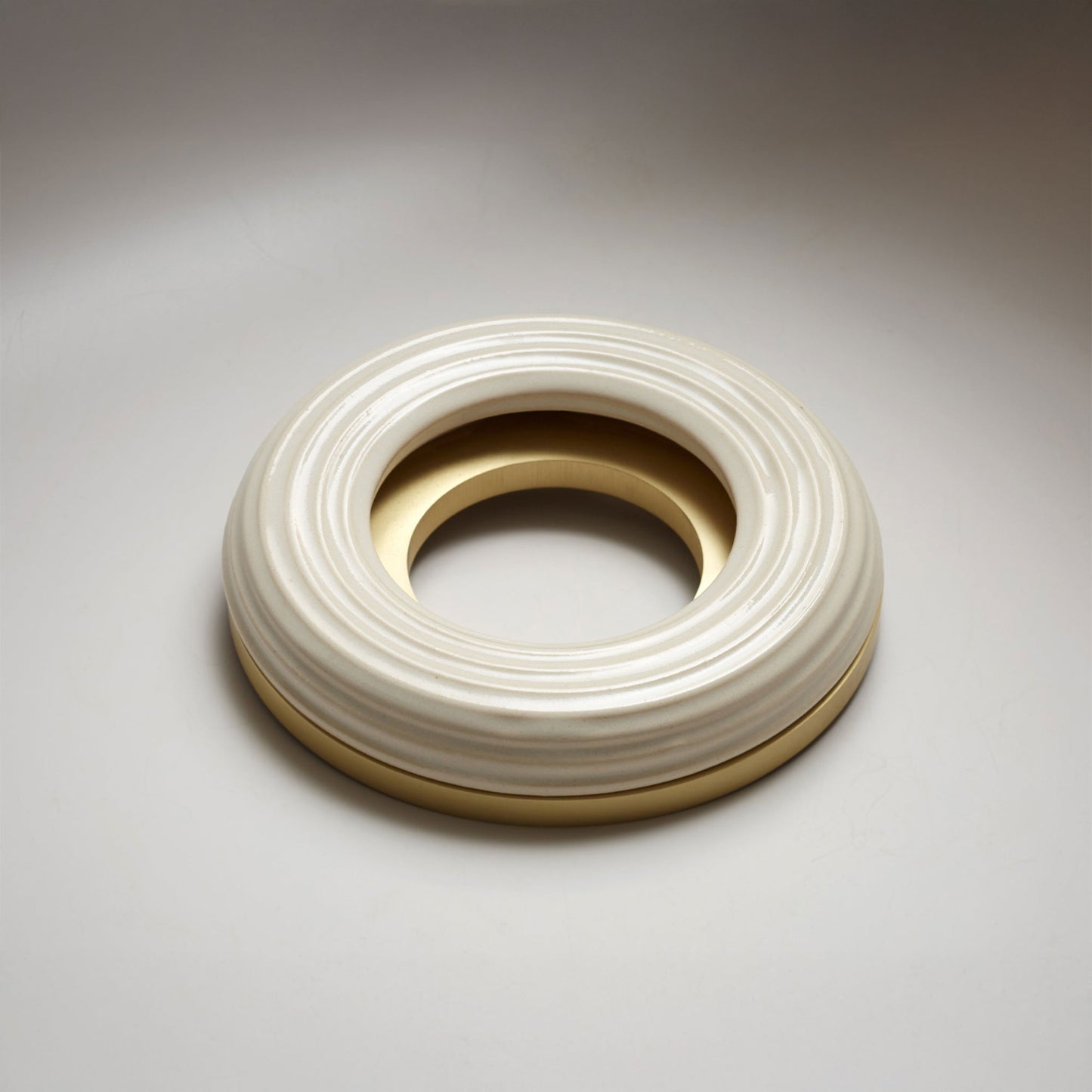 A large donut-shaped white ribbed ring with a polished gold-toned inner and outer rim, photographed on a light gray background.