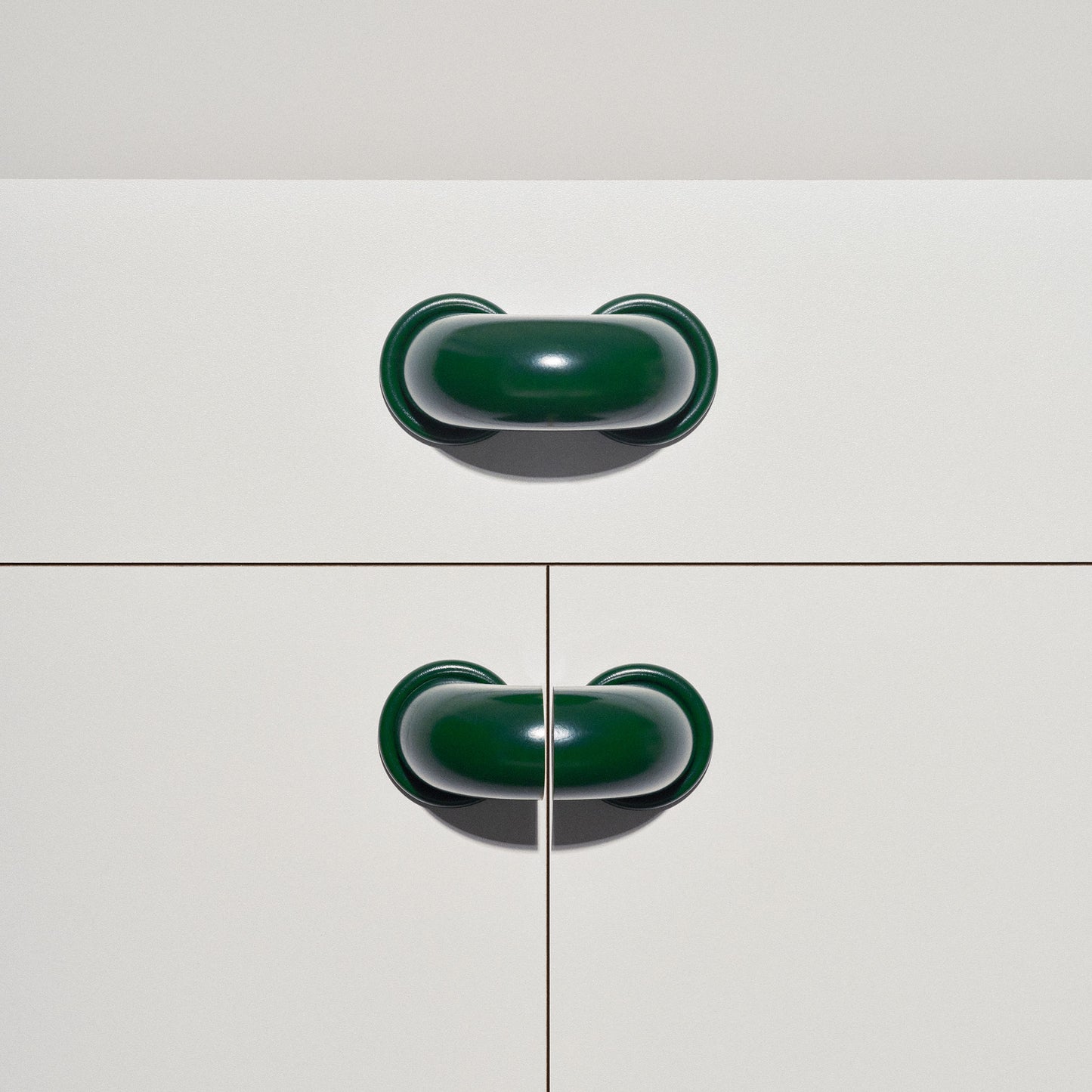White cabinet with dark green  macaroni-shaped handles on a white background