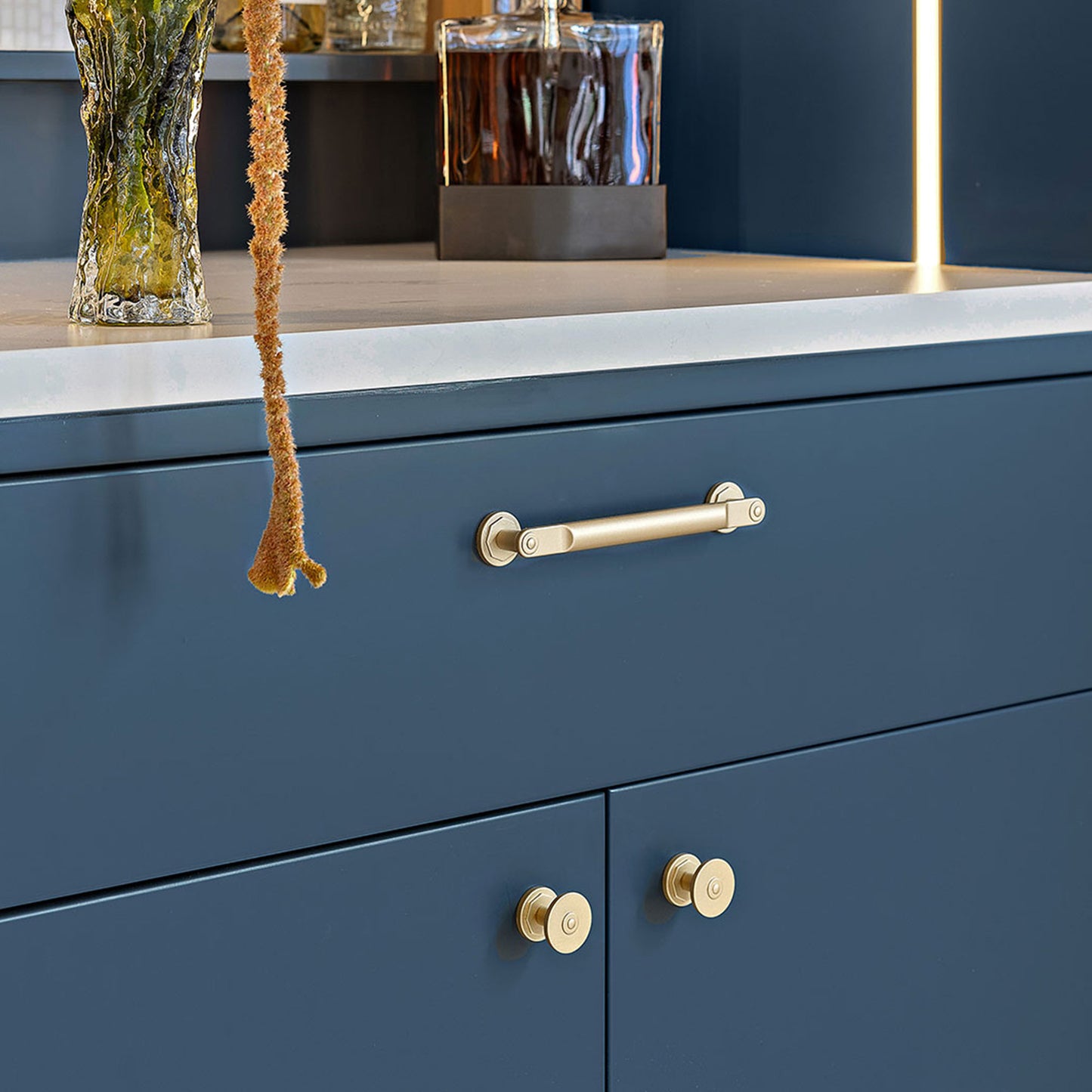 Blue cabinet with satin brass cabinet handles and decorative items on a shelf.