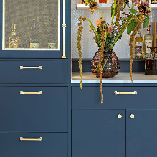 Blue cabinet with satin brass cabinet handles and decorative items on a shelf.