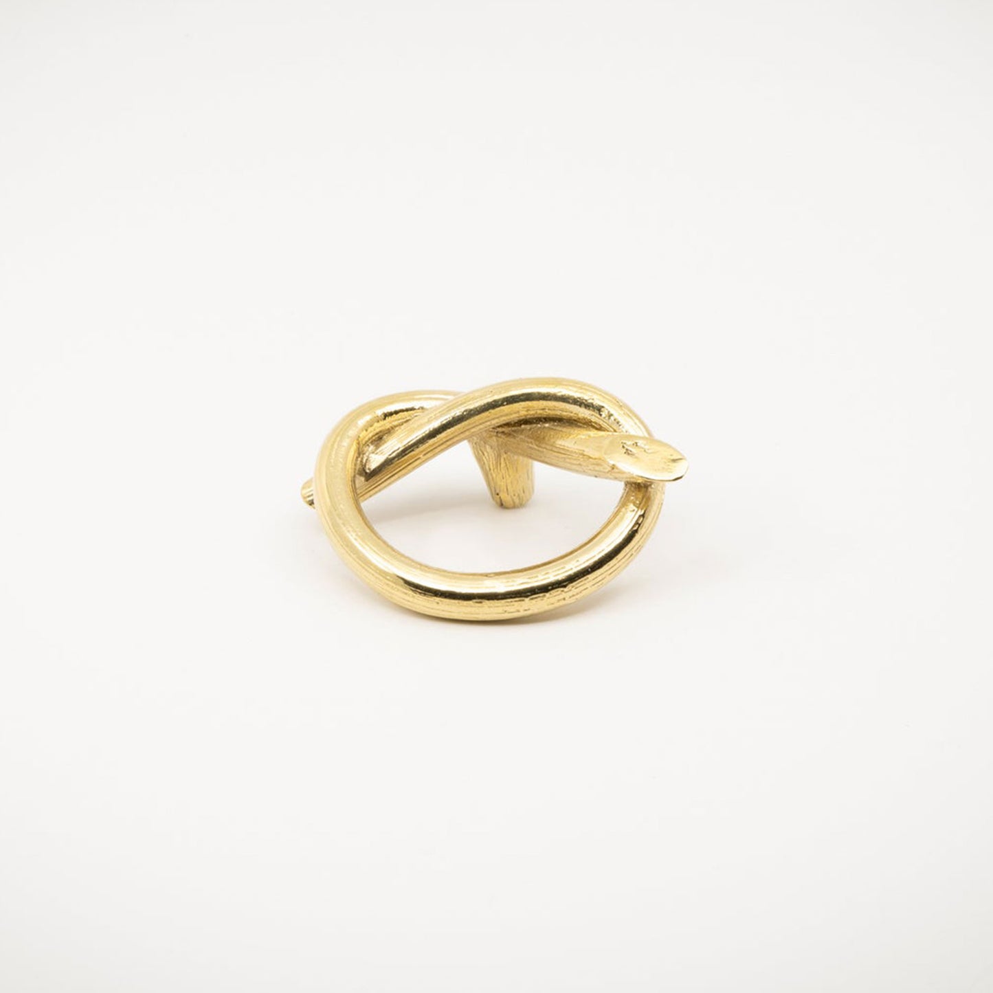 A gold-toned brass metal ring with a twisted knot design, photographed on a white background.