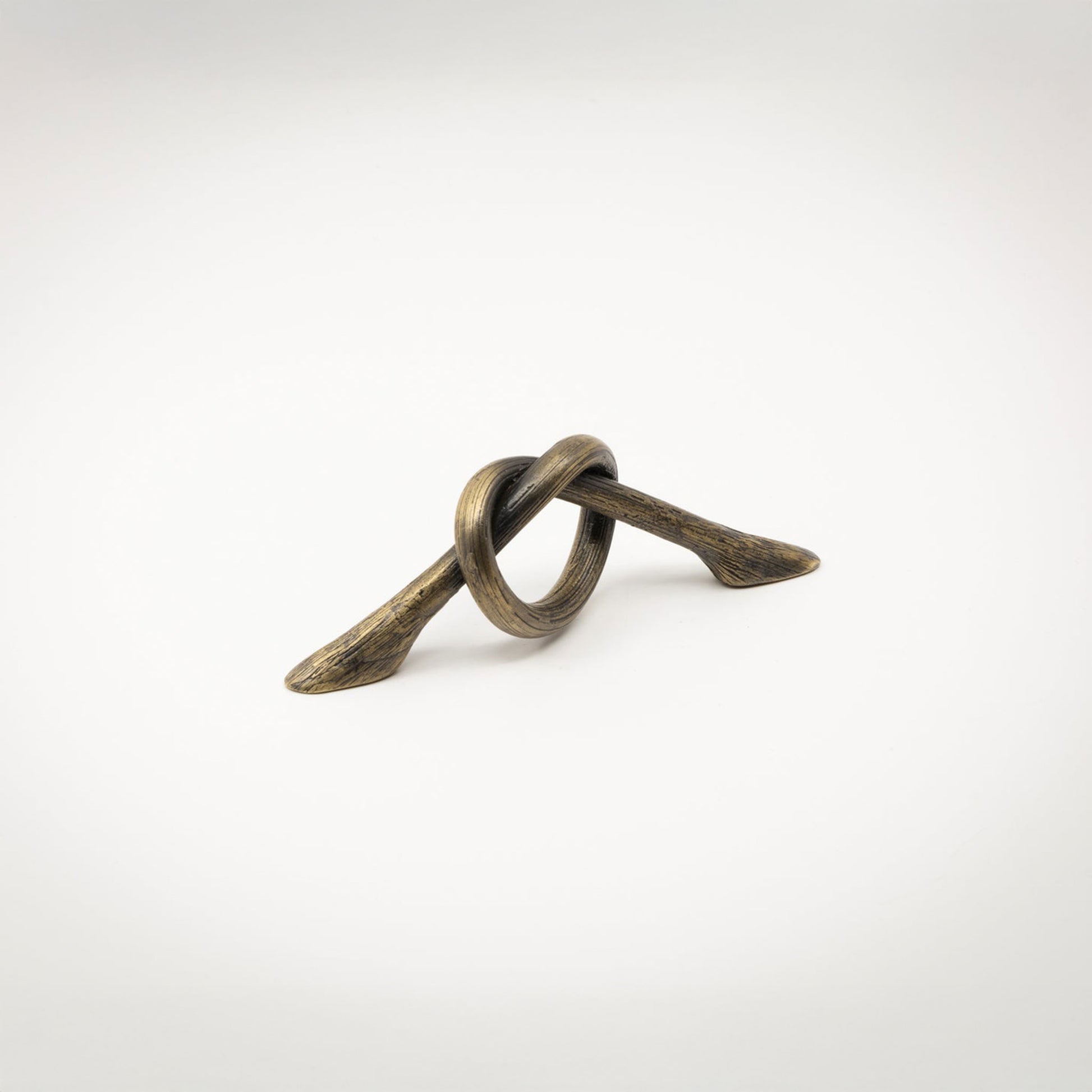 A small antique brass-toned metal hardware piece with a looped, knot-like design and two angled ends, photographed on a white background.