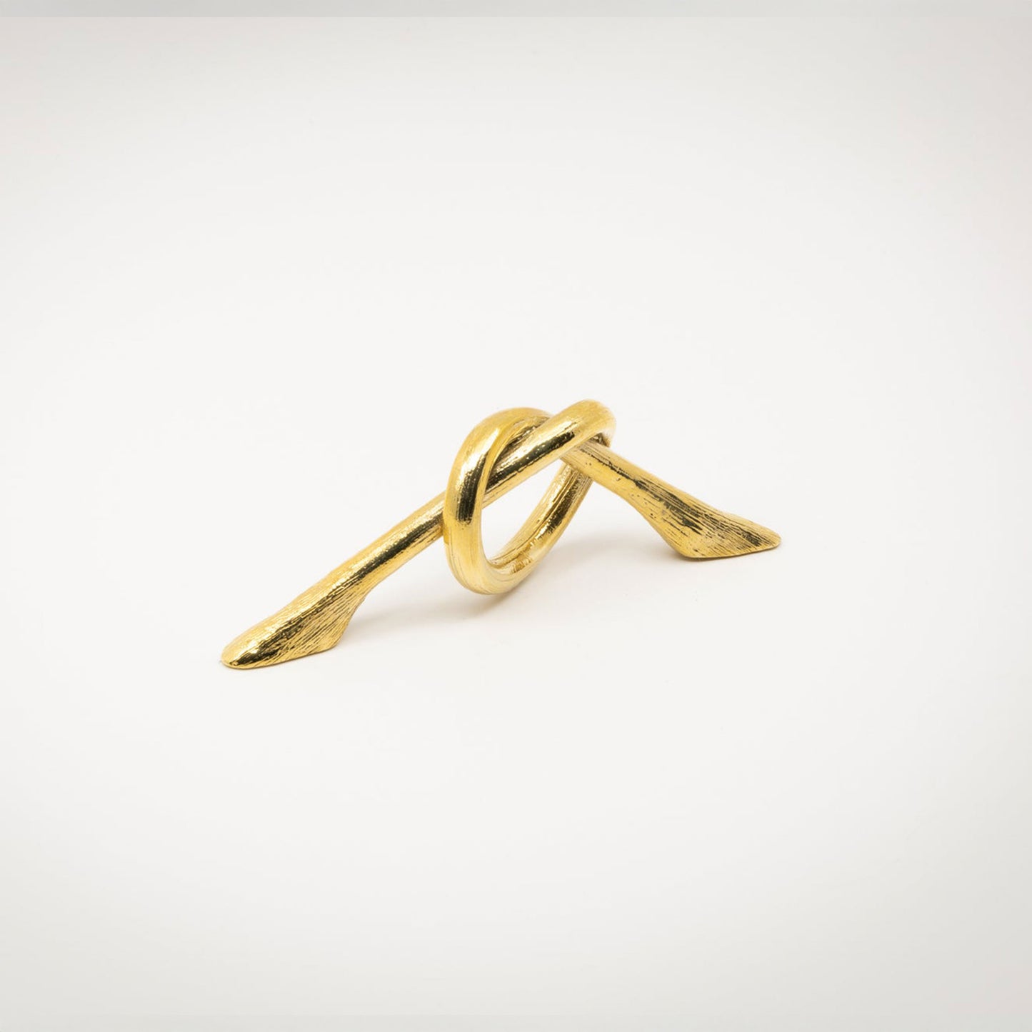 A small gold-toned polished brass metal hardware piece with a looped, knot-like design and two angled ends, photographed on a white background.