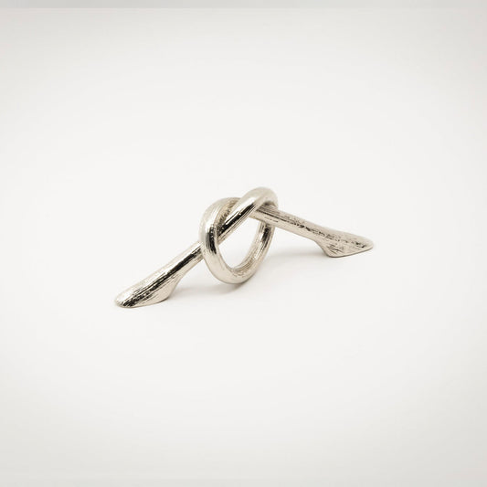 A small silver-toned polished nickel metal hardware piece with a looped, knot-like design and two angled ends, photographed on a white background.