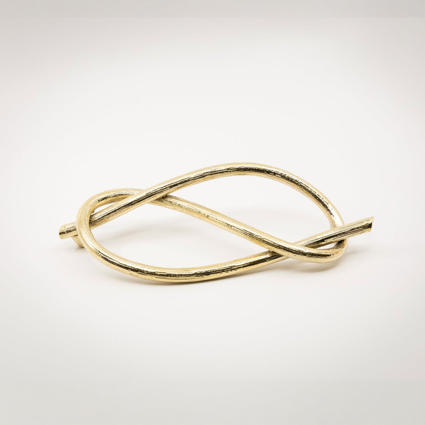 A twisted gold-toned brass metal sculptural cabinet pull with a textured bronze finish, photographed on a light gray background.