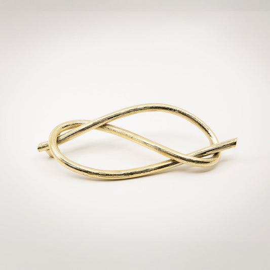 A twisted gold-toned brass metal sculptural cabinet pull with a textured bronze finish, photographed on a light gray background.