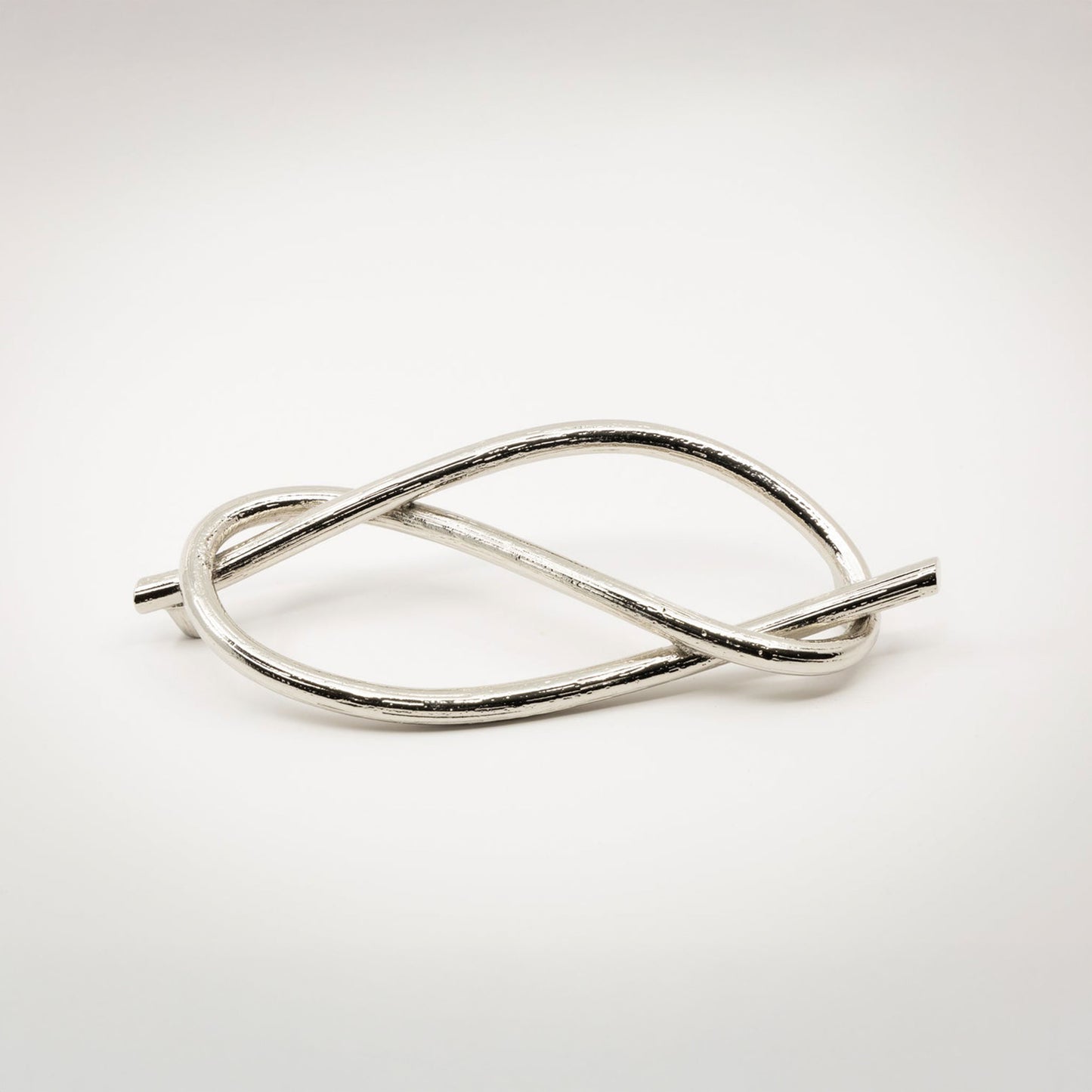 A shiny twisted silver-toned nickel metal sculptural cabinet pull with a textured bronze finish, photographed on a light gray background.