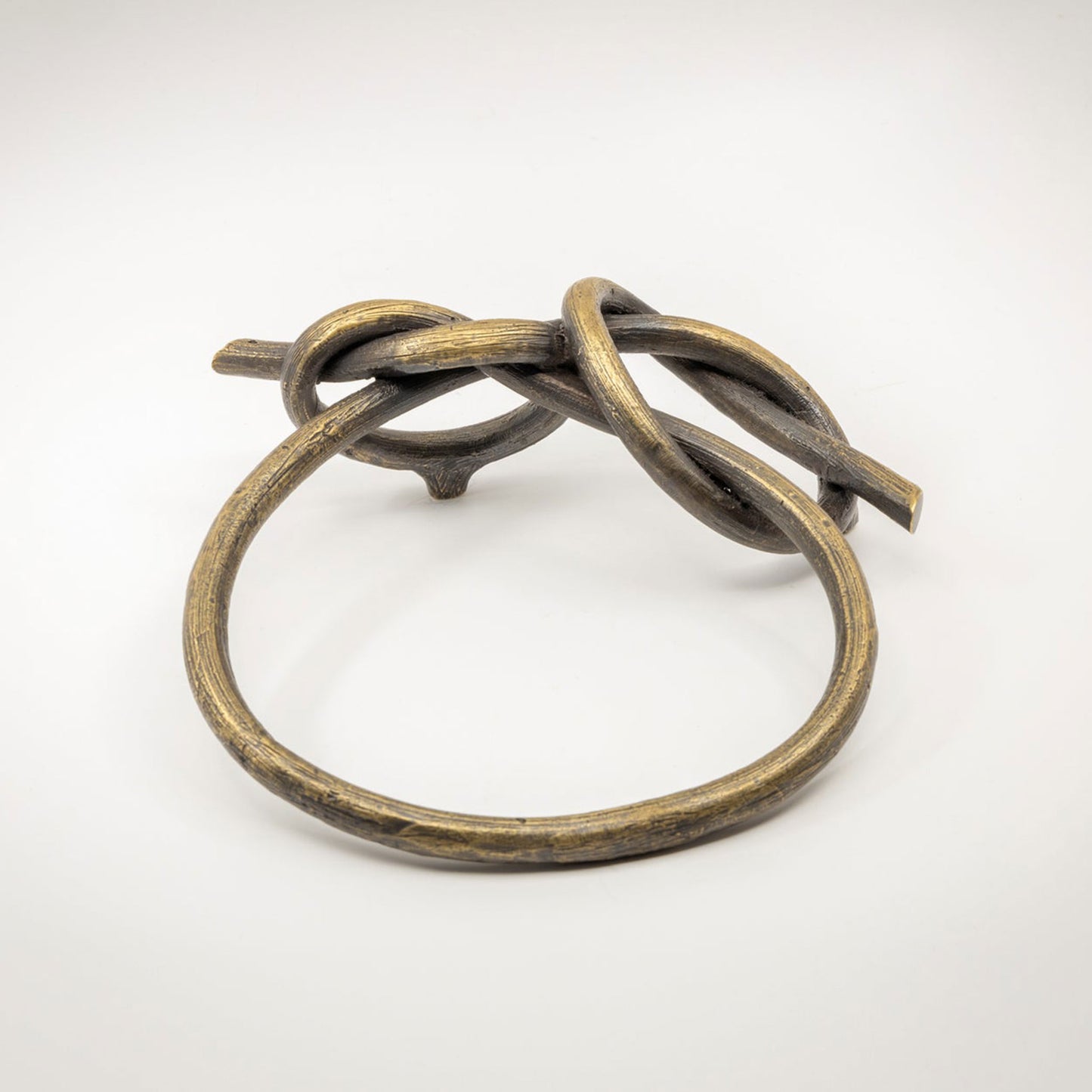 A large twisted brass-toned metal sculptural cabinet pull with a natural brass finish, photographed on a light gray background.