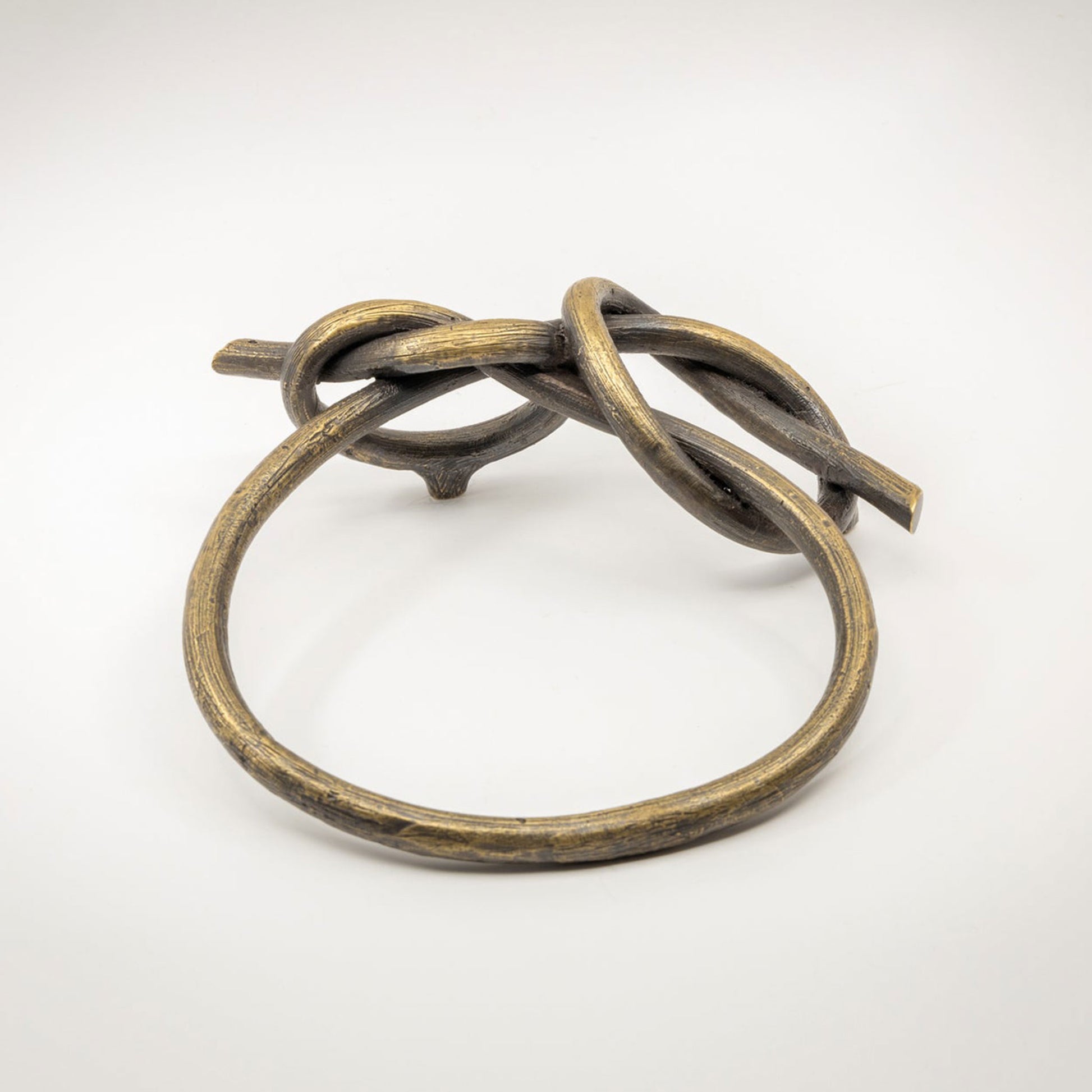 A large twisted brass-toned metal sculptural cabinet pull with a natural brass finish, photographed on a light gray background.