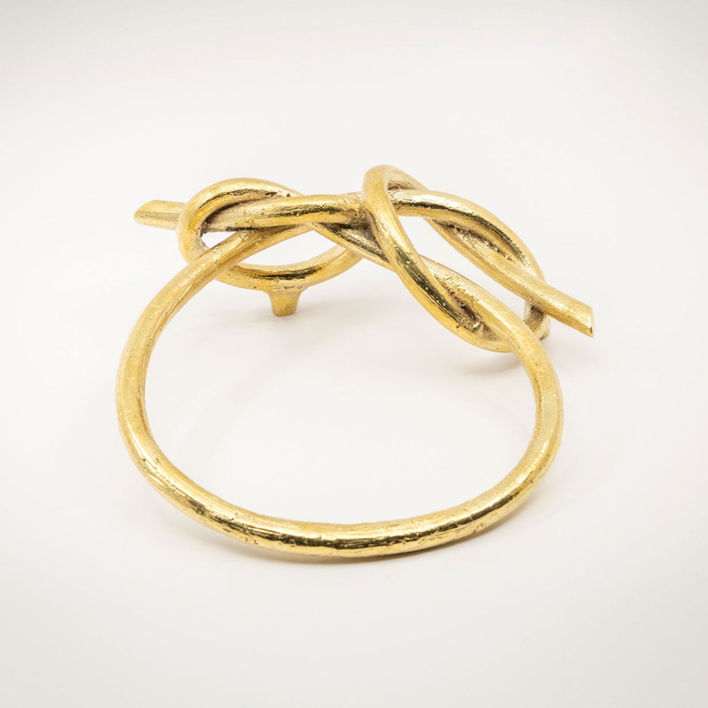 A large twisted gold-toned metal sculptural cabinet pull with a natural brass finish, photographed on a light gray background.