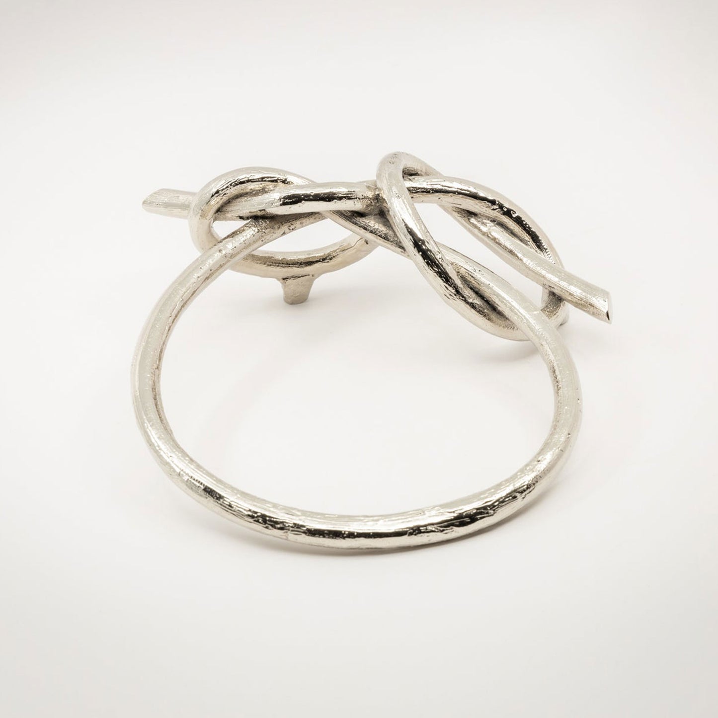 A large twisted silver-toned metal sculptural cabinet pull with a shiny nickel finish, photographed on a light gray background.
