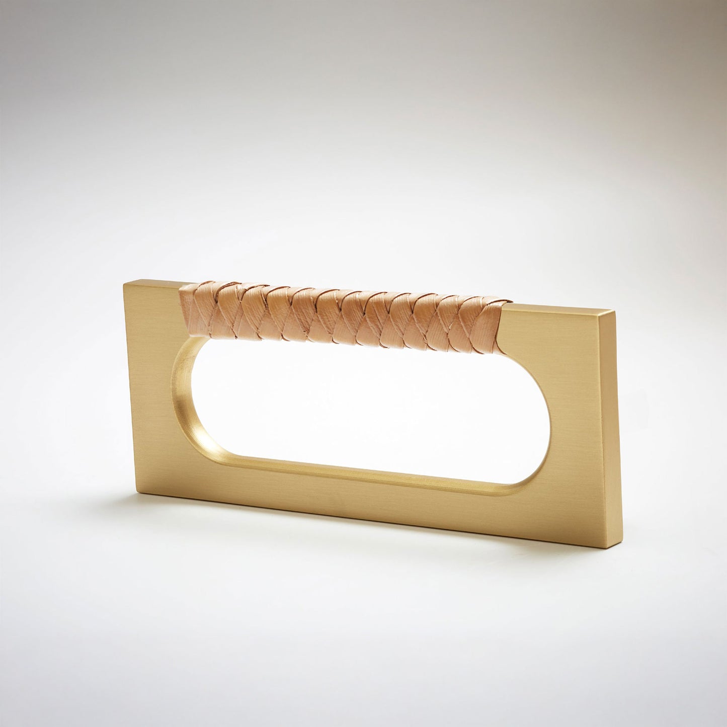 A modern rectangular cabinet pull handle with a satin brass finish and a textured woven brown leather handle, shown on a white background.