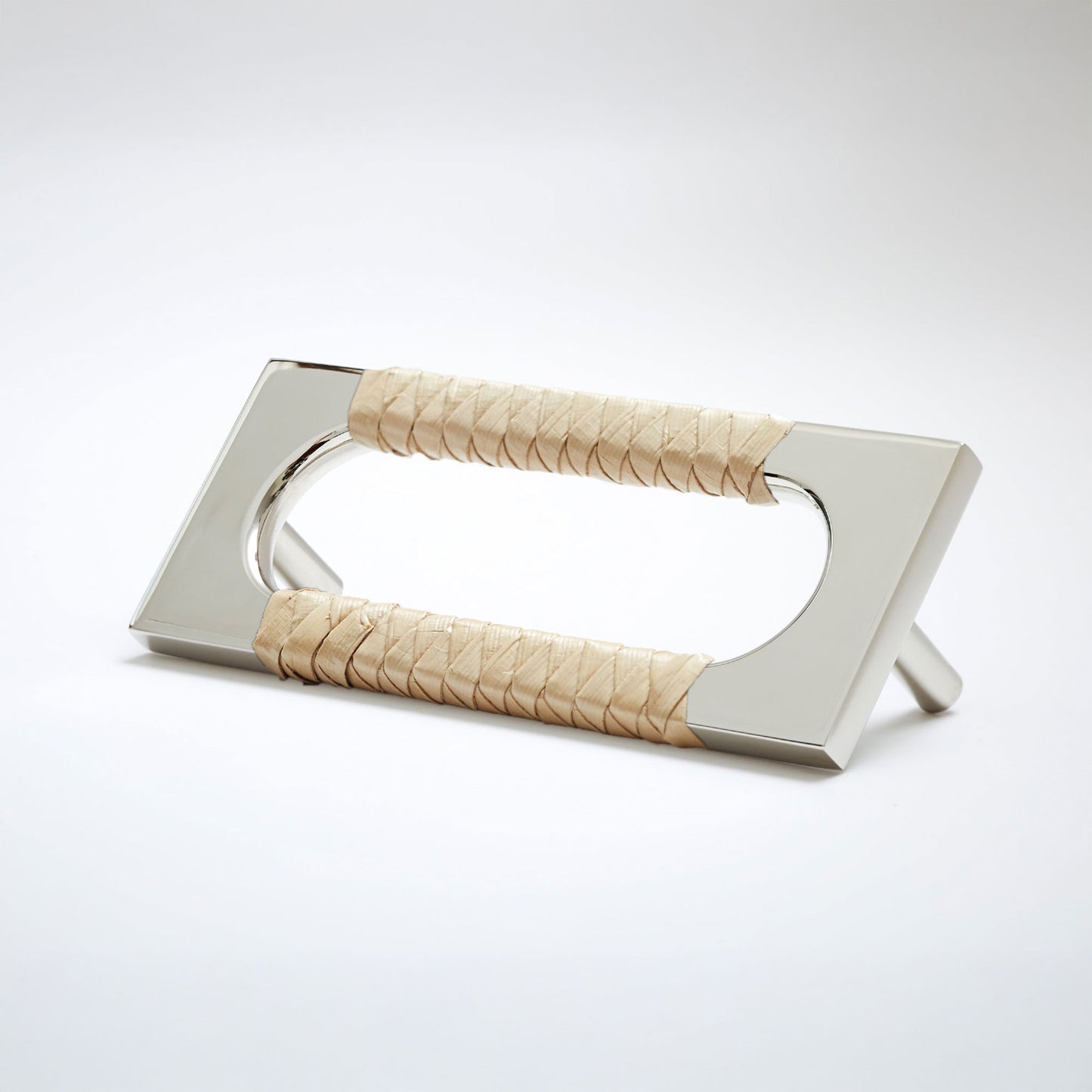 A modern polished nickel metal cabinet pull handle with an oval cutout, wrapped with a light colored natural beige screwpine leaf,  shown on a white background.
