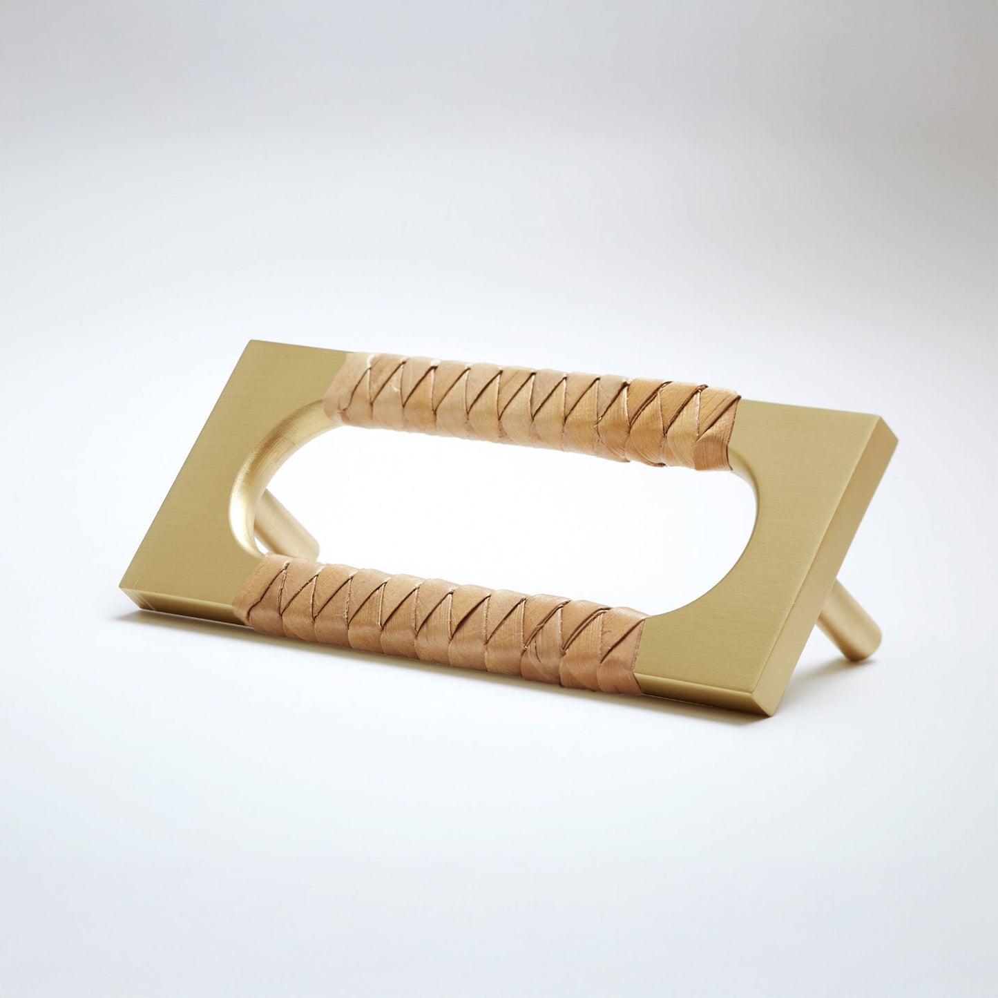 A modern satin brass cabinet pull handle with an oval cutout, wrapped with a natural brown screwpine leaf reed,  shown on a white background.