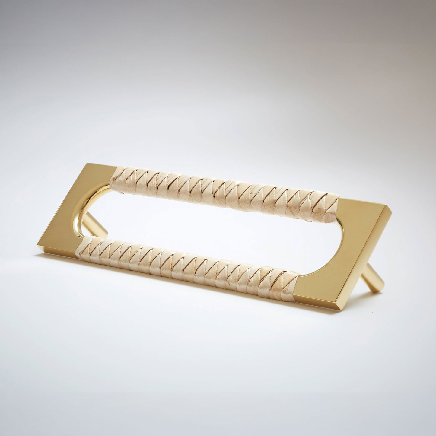A modern brass door pull handle featuring a textured beige woven leather grip, shown on a clean light gray background.
