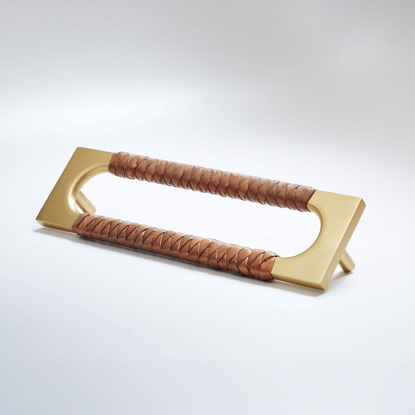 A modern rectangular pull handle with a brushed gold metal frame and two wrapped brown leather grips, shown on a clean light gray studio background.