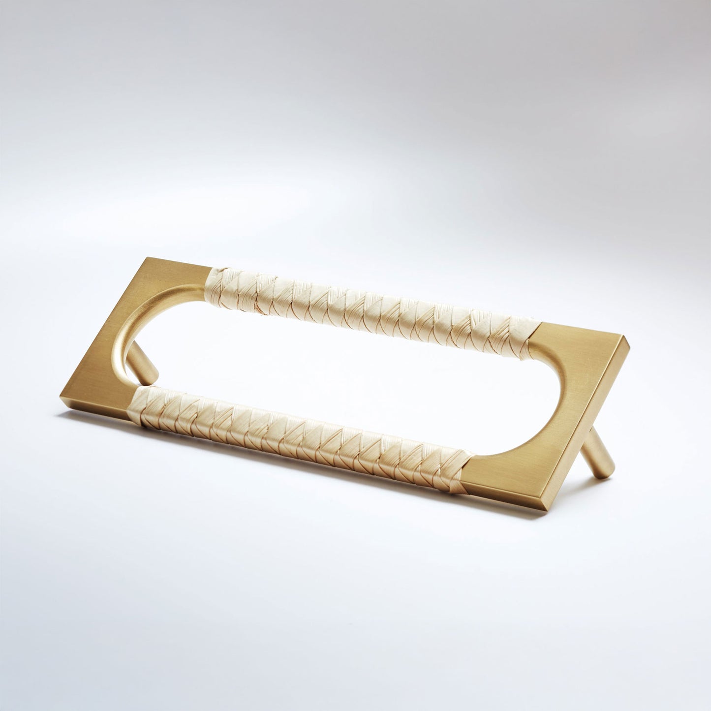 A modern rectangular pull handle with a brushed gold metal frame and cream-colored woven leather wrapped grips, shown on a light gray studio background.