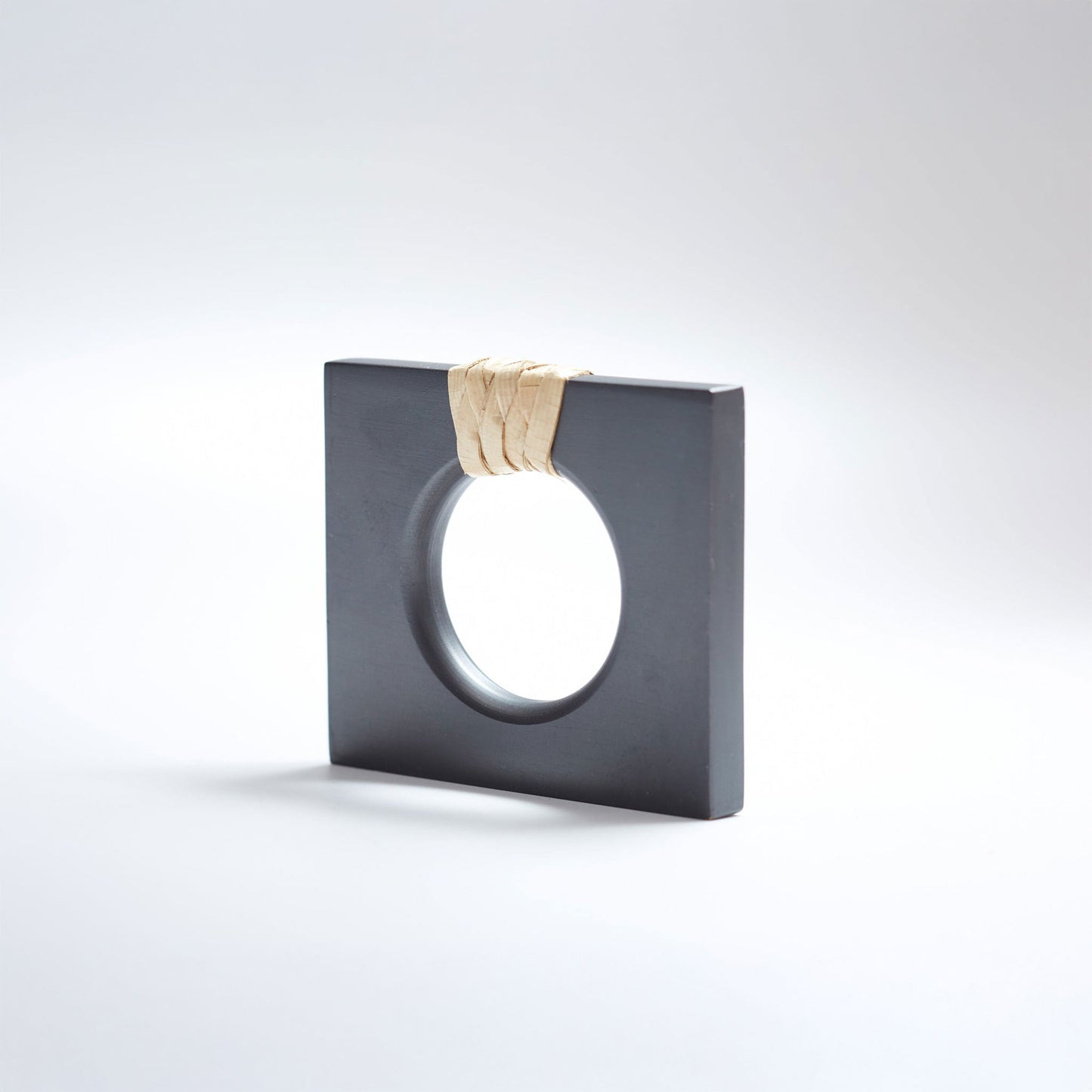 A petite square dark gray ring-shaped cabinet knob with a circular cutout, featuring a light natural beige woven cord wrapped around the top edge, set against a white background. 
