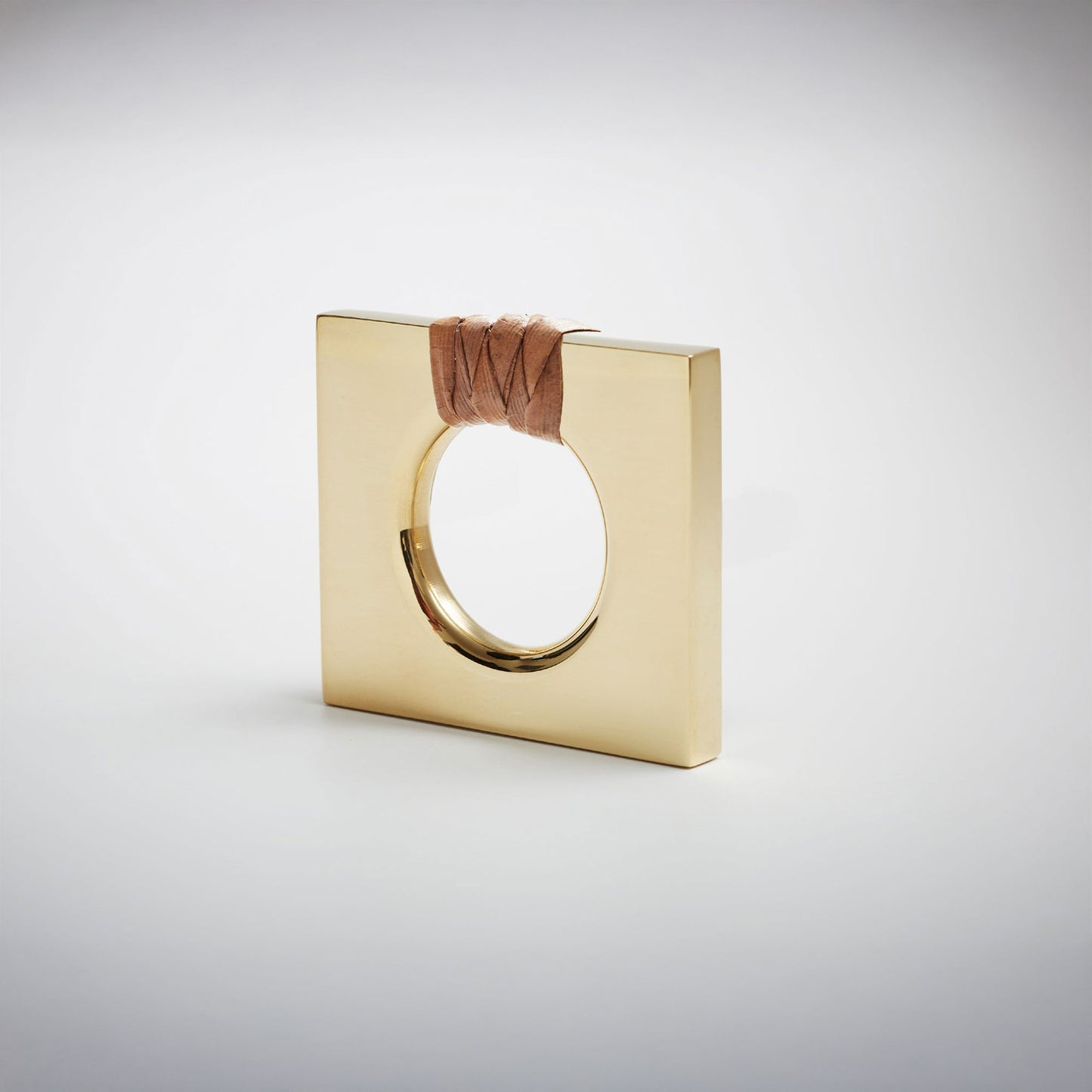 A petite square natural brass ring-shaped cabinet knob with a circular cutout, featuring a dark brown natural woven cord wrapped around the top edge, set against a white background. 