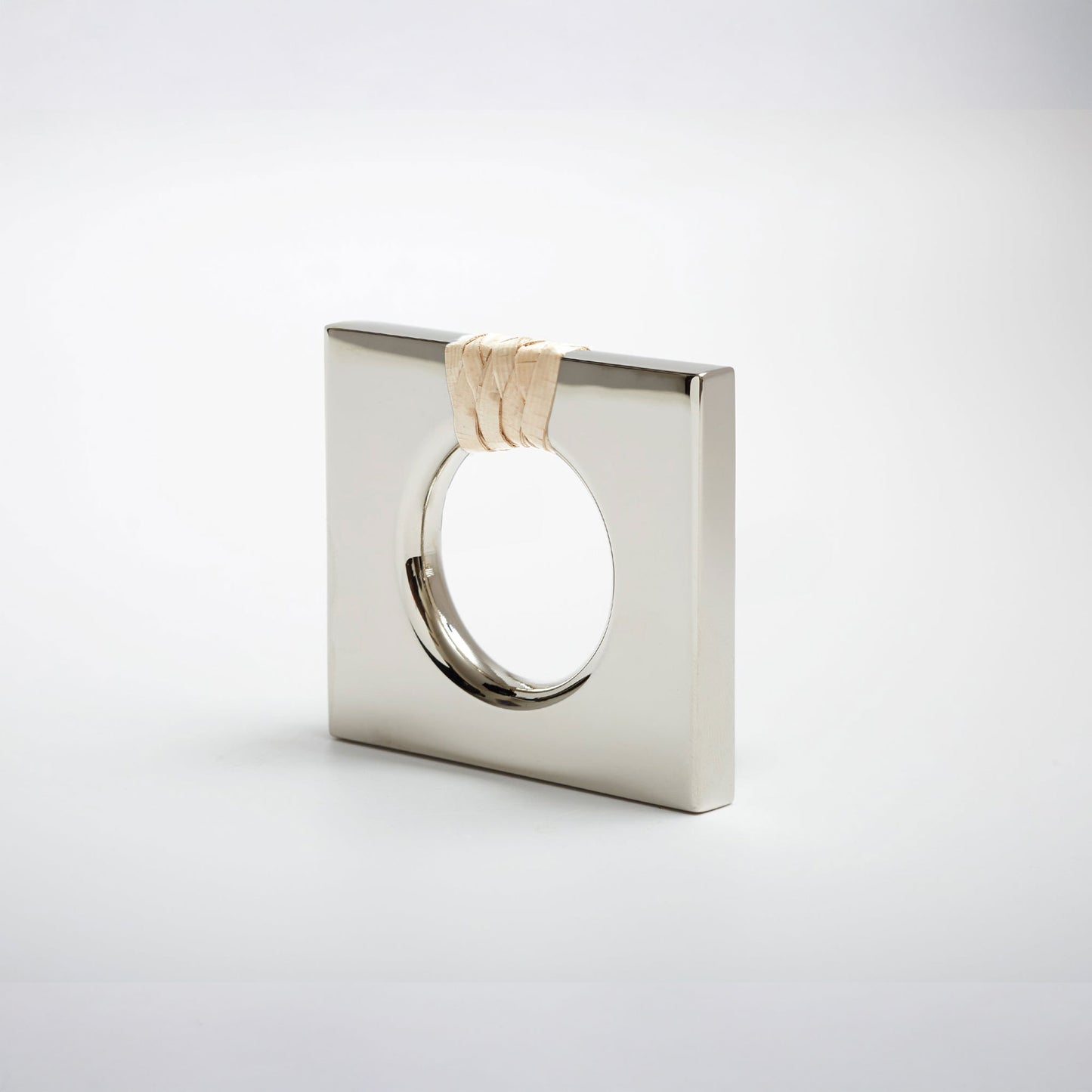 A petite square-shaped polished nickel cabinet knob with a circular cutout, featuring a light natural woven cord wrapped around the top edge, set against a white background. 