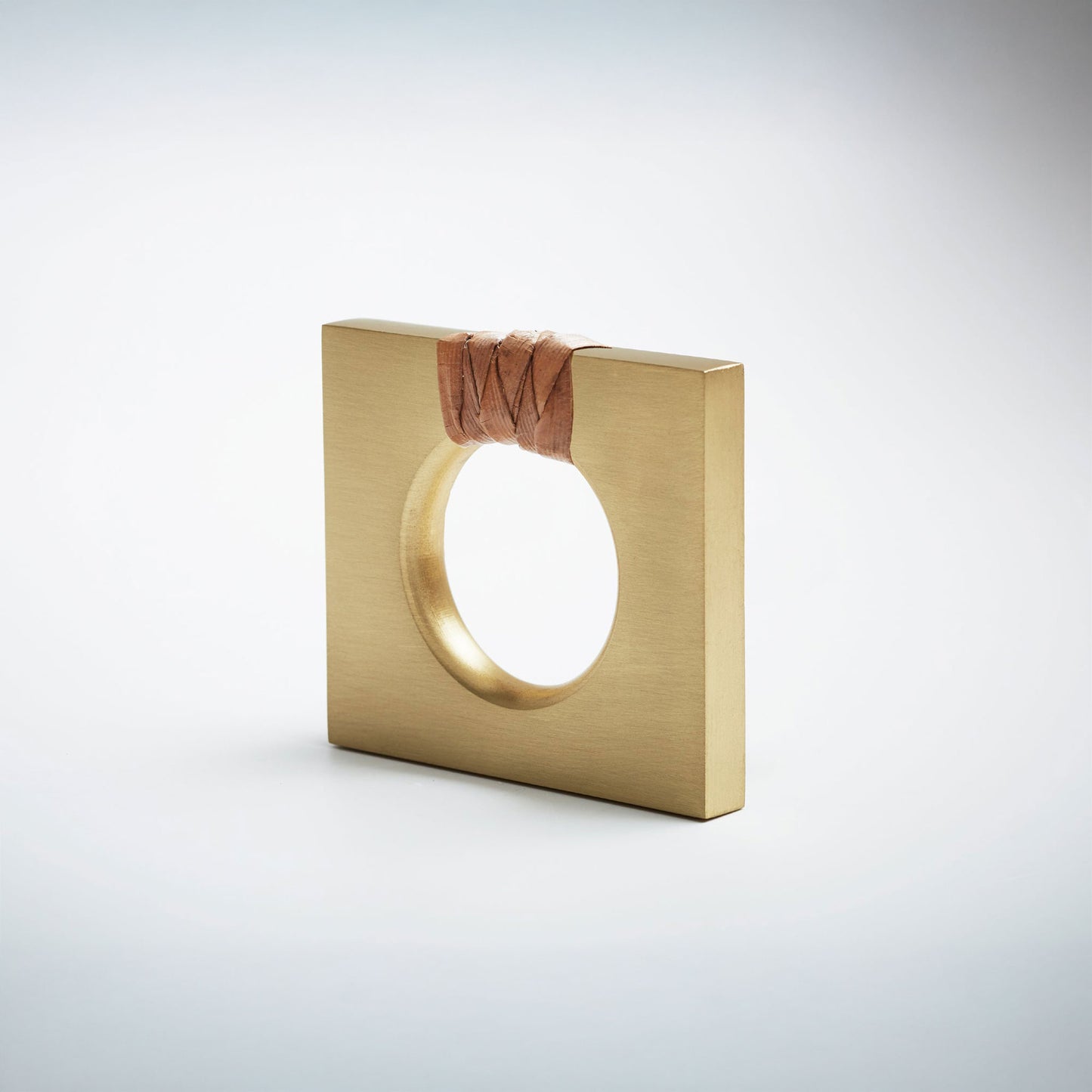 A petite square satin brass ring-shaped cabinet knob with a circular cutout, featuring a dark brown natural woven cord wrapped around the top edge, set against a white background. 