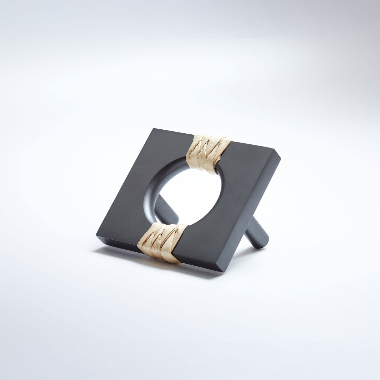 A dark gray oil rubbed brass metal geometric cabinet pull with a square frame and circular center, wrapped with a light natural leather at the corners, shown on a white background.