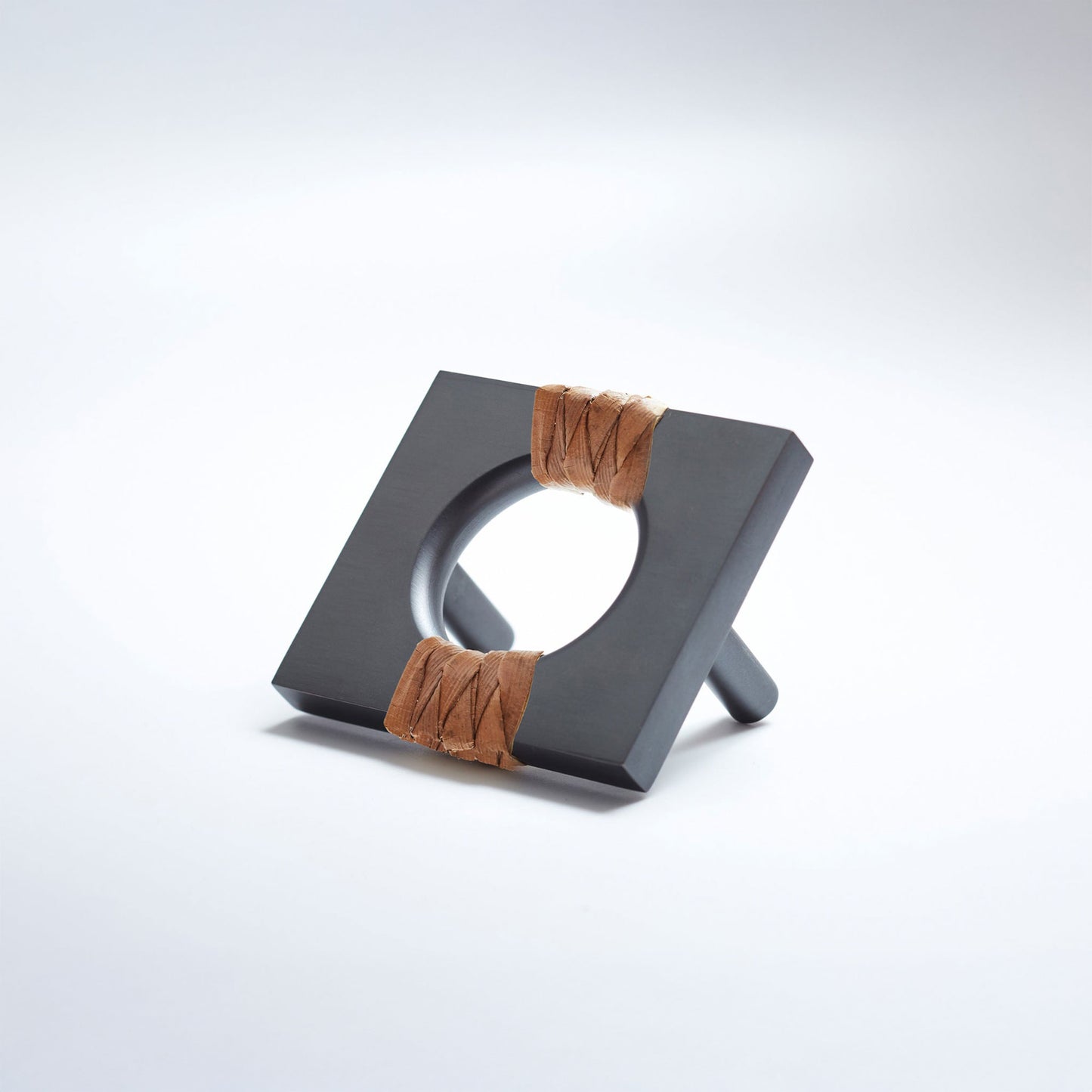 A oil-rubbed dark bronze geometric cabinet pull with a square frame and circular center, wrapped with brown pine reed on two sides, shown on a white background.