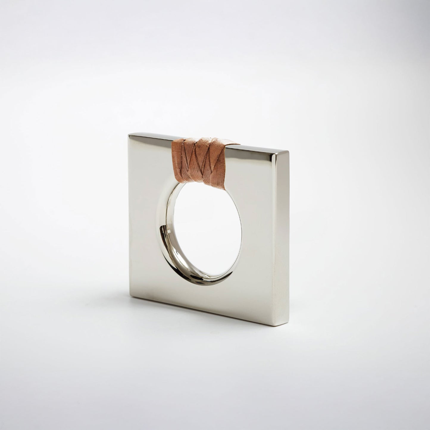 A petite square-shaped polished nickel cabinet knob with a circular cutout, featuring a dark brown natural woven cord wrapped around the top edge, set against a white background. 