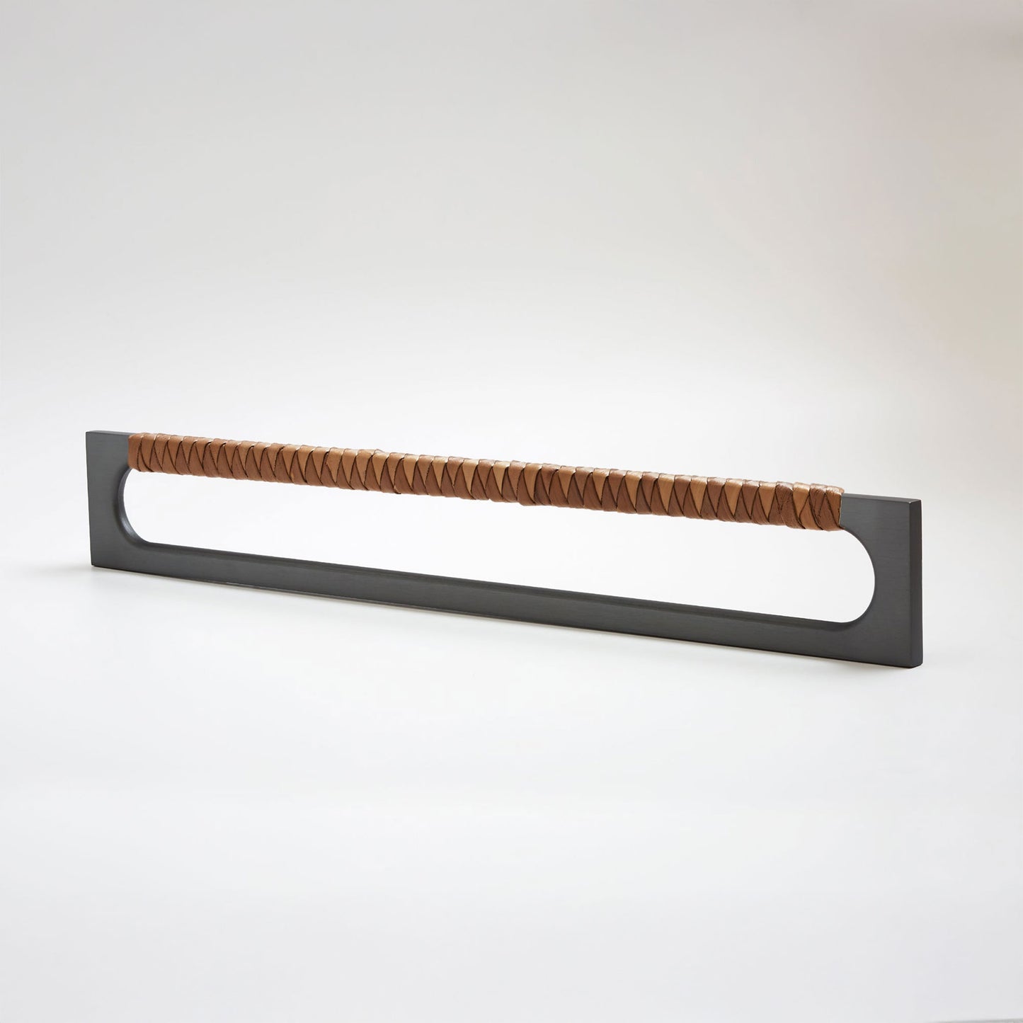 A modern long rectangular cabinet pull handle with a dark oil-rubbed bronze metal frame with an oval shaped-cutout and a brown leather woven grip, shown on a white background.