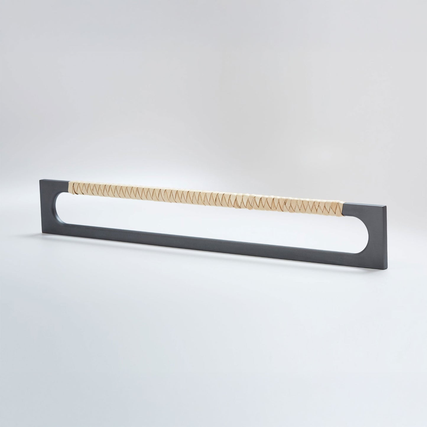 A modern long rectangular cabinet pull handle with a dark oil-rubbed bronze metal frame with an oval shaped-cutout and a light tan leather woven grip, shown on a white background.