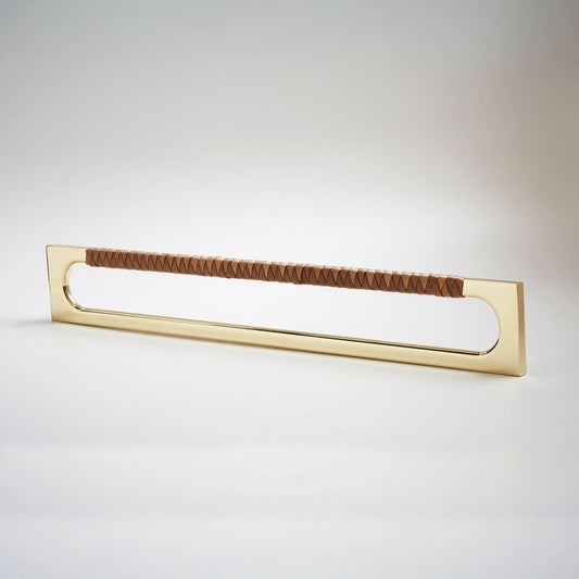 A modern long rectangular cabinet pull handle with a natural brass metal frame with an oval shaped-cutout and a brown leather woven grip, shown on a white background.