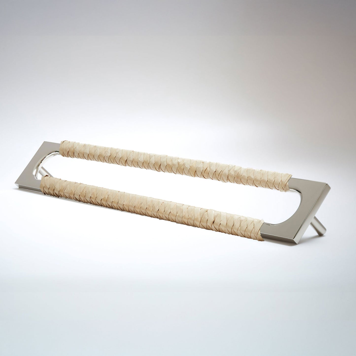 A modern long rectangular cabinet pull handle with a polished nickel metal frame with an oval shaped-cutout and a light tan leather woven grip, shown on a white background.