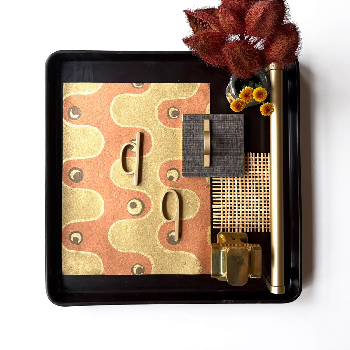 a design flat lay with various textured fabrics and wood finishes and including bronze loop shaped pulls along side a unlacquered brass cross shaped door knob on a white background.