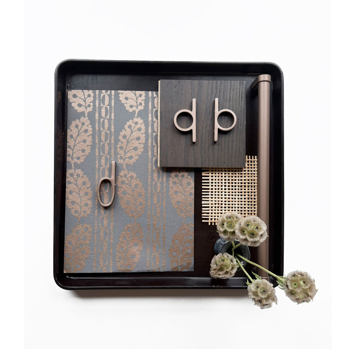 a design flat lay with various textured finish samples and including bronzed copper loop shaped knobs and pulls along side a matched finish appliance pull on a wooden tray on a white background.