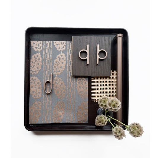 a design flat lay with various textured finish samples and including bronzed copper loop shaped knobs and pulls along side a matched finish appliance pull on a wooden tray on a white background.