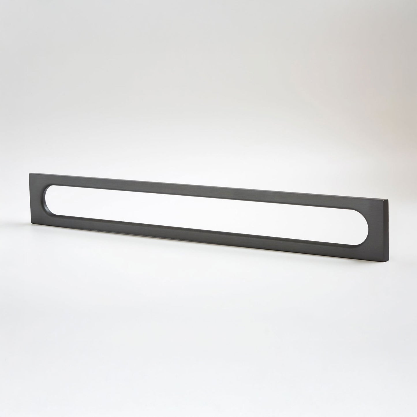A long, rectangular matte black metal cabinet pull with a horizontal oval cutout, photographed on a clean light gray studio background.
