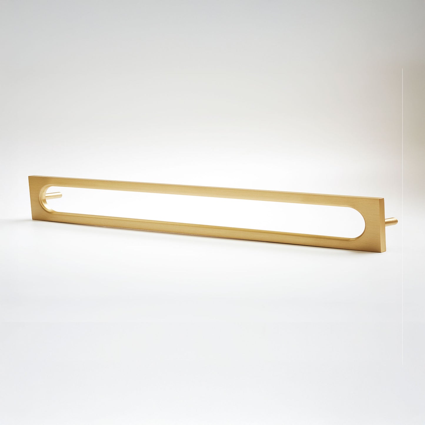 A modern linear cabinet pull in a brushed gold finish, featuring a long rectangular frame with an open center that reveals a bright white light tube, set against a clean white background.