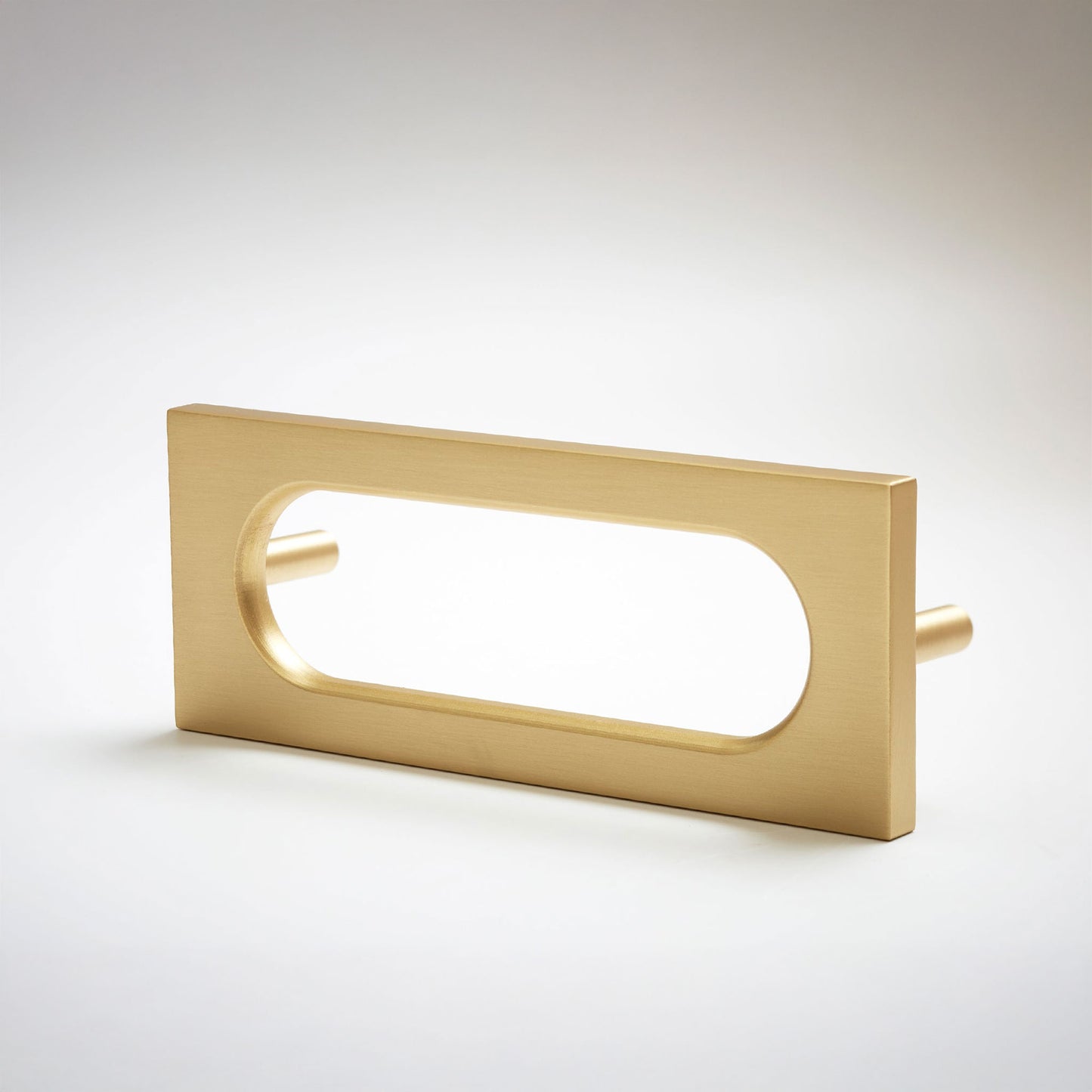 A modern rectangular pull handle with an elongated oval cutout, finished in brushed gold metal, shown on a light gray gradient background.