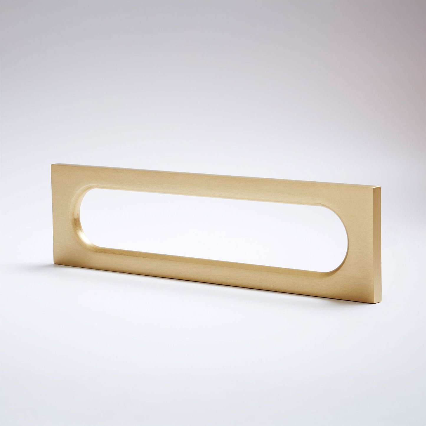 A modern rectangular pull handle with a rounded horizontal slot, finished in brushed brass, shown on a clean light gray background.