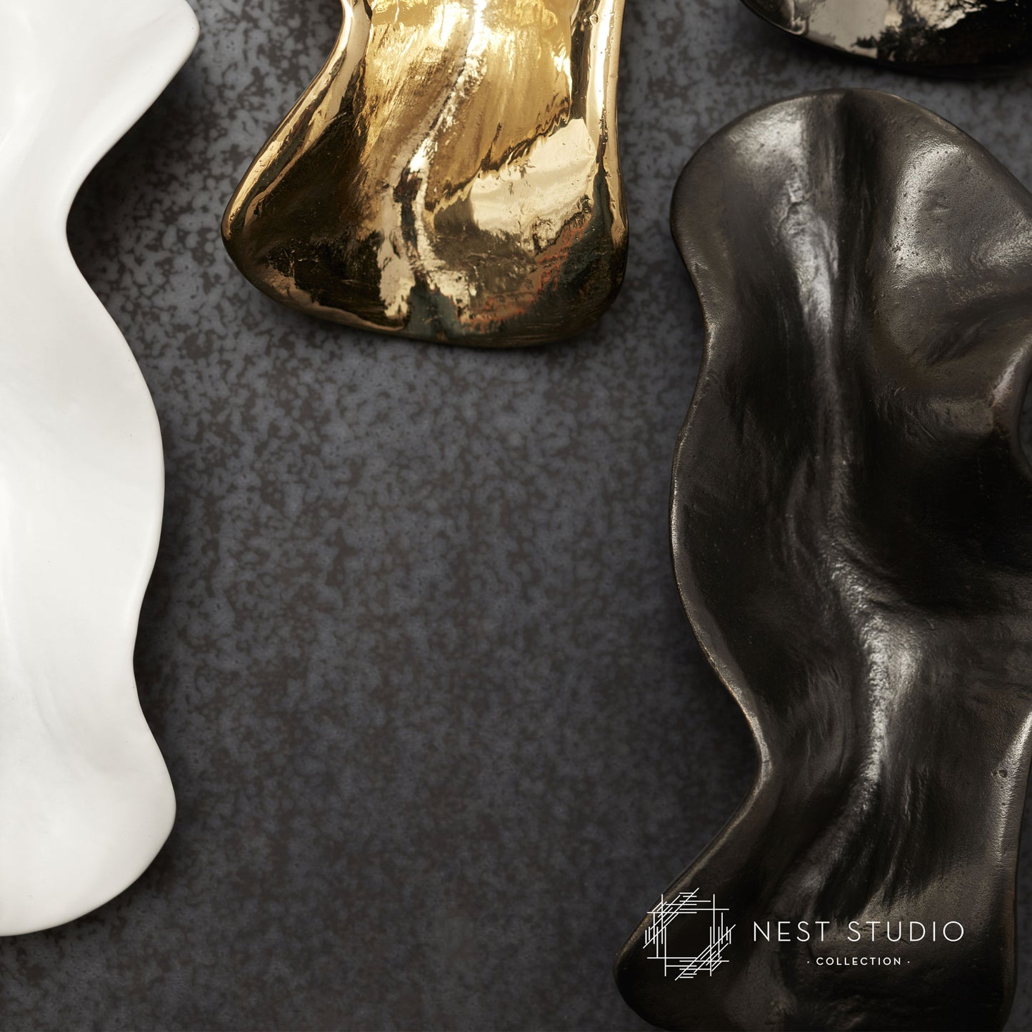Abstract organic-shaped cabinet pulls in white, gold, and black on a dark textured surface, with the NEST STUDIO COLLECTION logo in the bottom right corner.