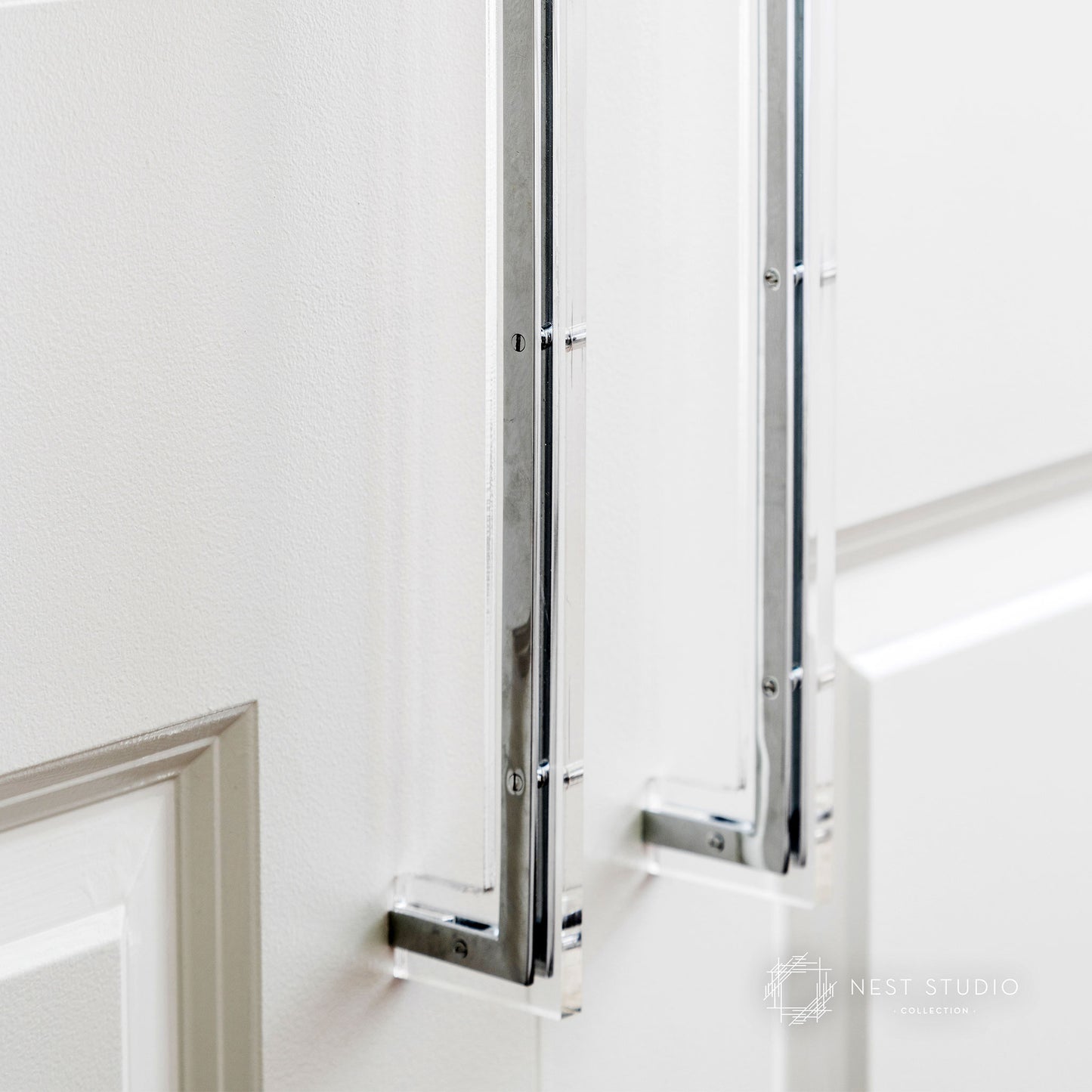 A close-up of a modern, slim chrome door handle mounted on a white paneled door, with a second matching handle visible in the background.