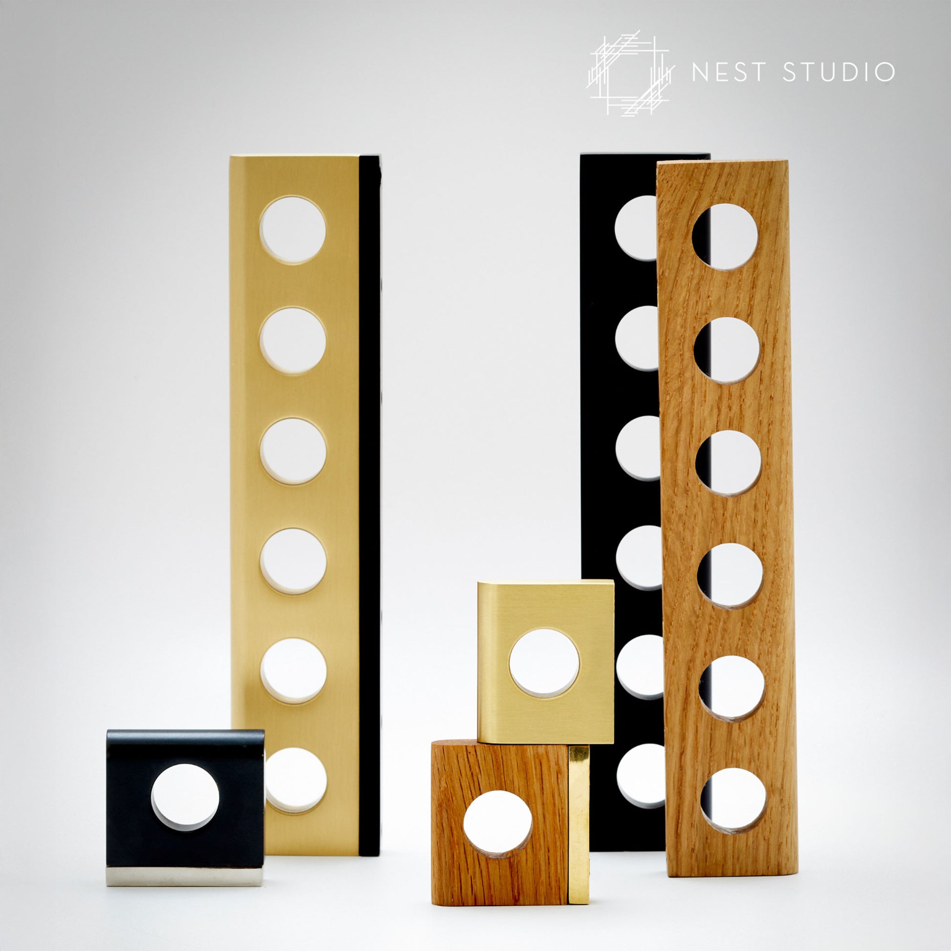 A set of modern decorative architectural cabinet pulls by Nest Studio, featuring rectangular panels with circular cutouts in black, gold, and natural wood finishes, arranged on a light gray background.