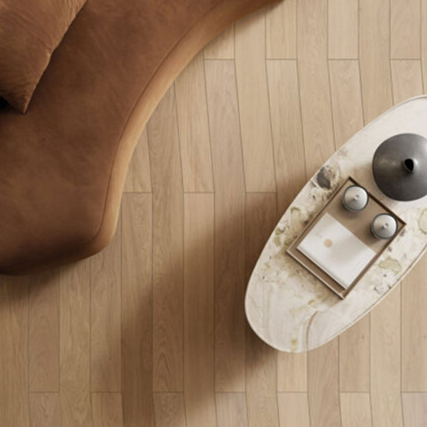 Round marble coffee table with decorative items on a wooden floor next to a brown sofa.