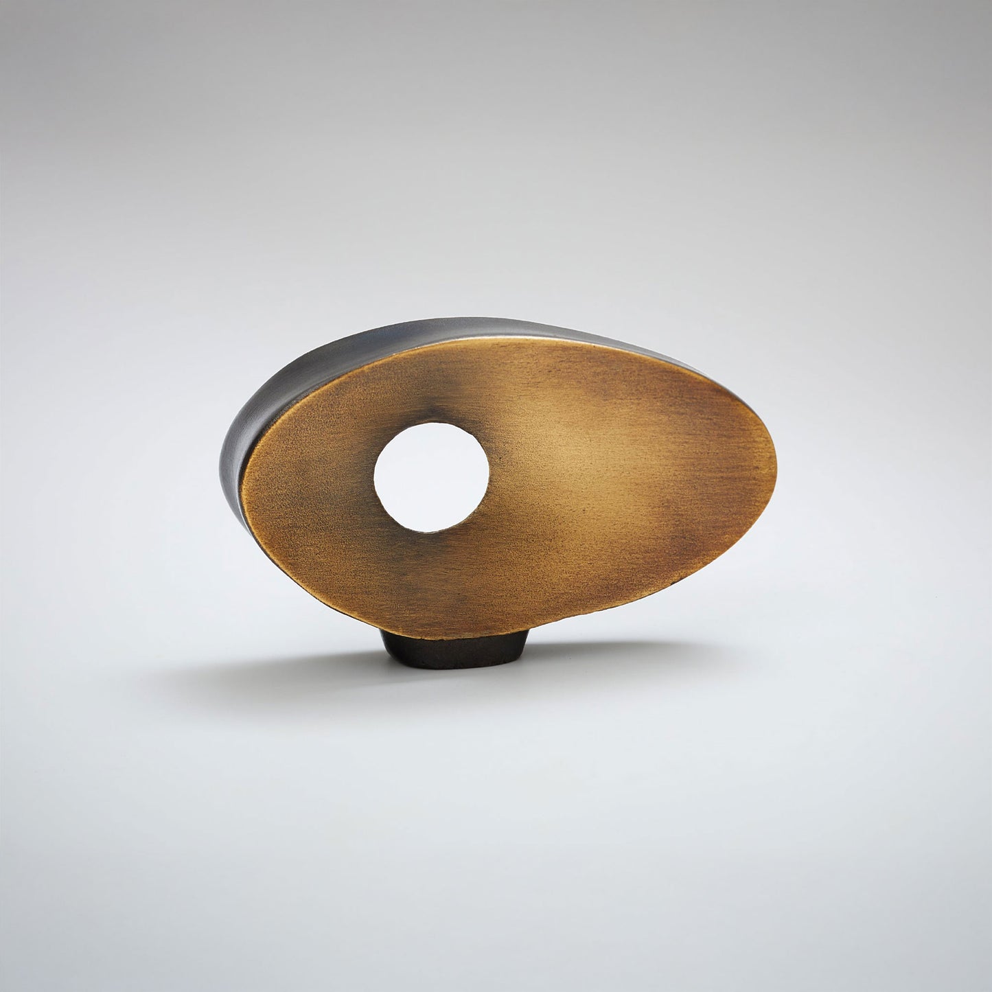 A modern oval cabinet knob with a brushed brass gold face, a central cutout, and a dark metallic back and base, shown on a light gray background.