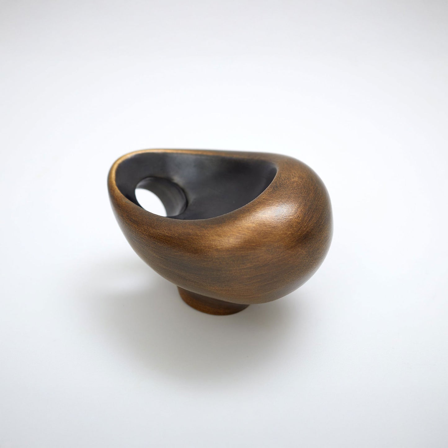 A small sculptural cabinet knob with a rounded organic shape, featuring a warm metallic bronze exterior and a dark black interior, set against a clean white background.