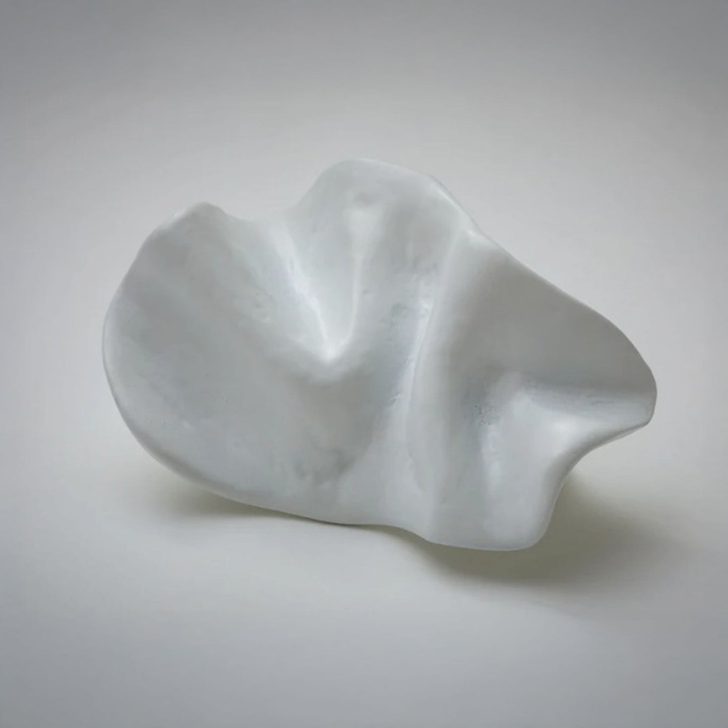 An organic-shaped cabinet pull with a glossy, wavy surface, photographed on a neutral light gray background.