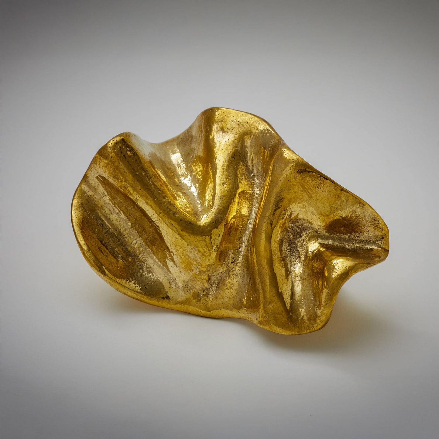 An organic-shaped cabinet pull with a glossy, wavy surface, photographed on a neutral light gray background.